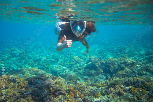 Woman with loose hair show thumb up underwater. Snorkeling in tropical sea coral reef. Undersea photo of coral reef.