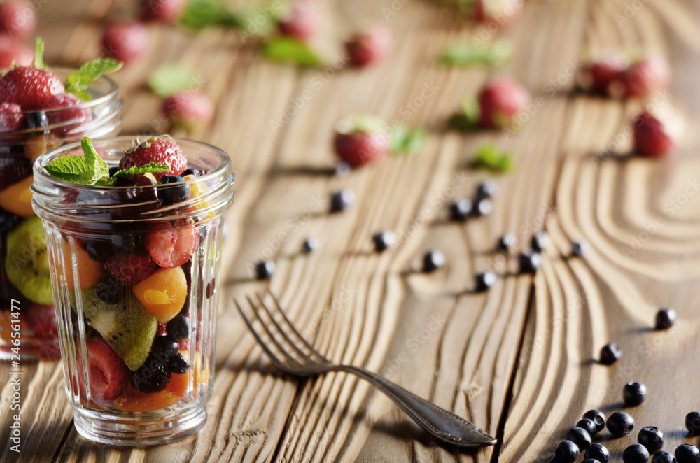 Assorted berries in mason jar on kitchen wooden table with fork aside Assorted berries in mason jar on kitchen wooden table with fork aside