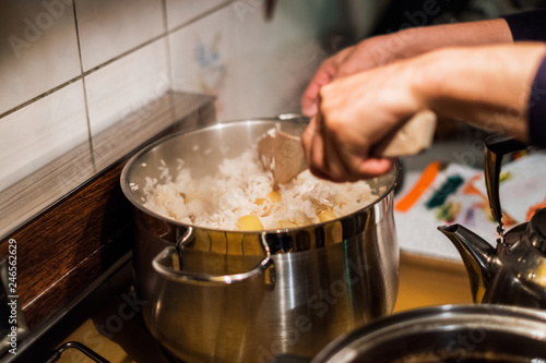 Hand chef using wooden flipper mixing rice with potato in pot