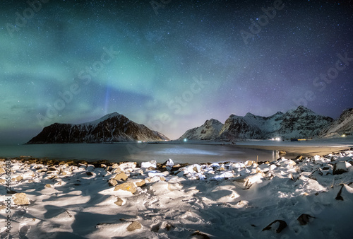 Panorama of Aurora borealis with stars over mountain range with snowy coastline