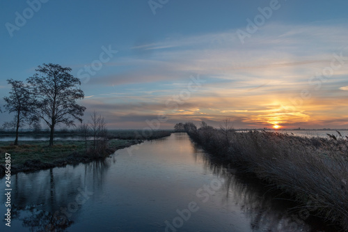Sunrise above a ditch and a lake dike silhouettes of trees. Reeuwijk The Netherlands Europe. © Karin Reine