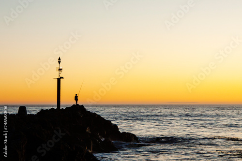 Lone fisherman on a rock pier with a sunrise 