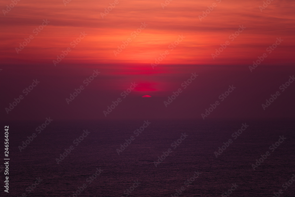 Sunset over ocean horizon photographed with big telephoto lens.