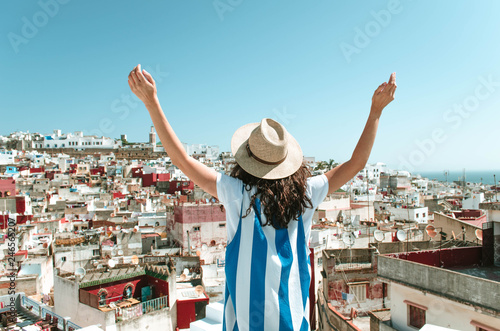 Tourist on vacation in Morocco. Woman with open arms with expression of freedom and enjoyment. Girl with hut and white and blue dress on a Tangier terrace