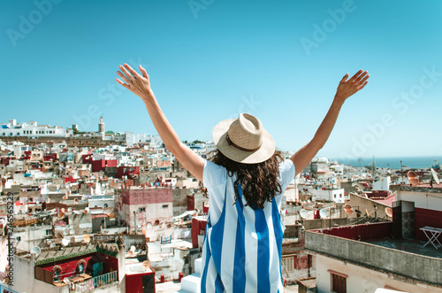 Tourist on vacation in Morocco. Woman with open arms with expression of freedom and enjoyment. Girl with hut and white and blue dress on a Tangier terrace