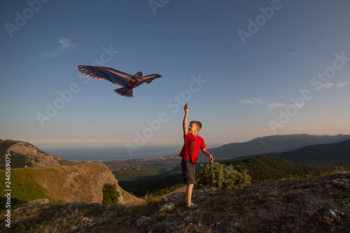 Kite flying. The boy launches a kite. Beautiful sunset. Mountains, sea, landscape. The boy in the red t-shirt and shorts. Summer day.