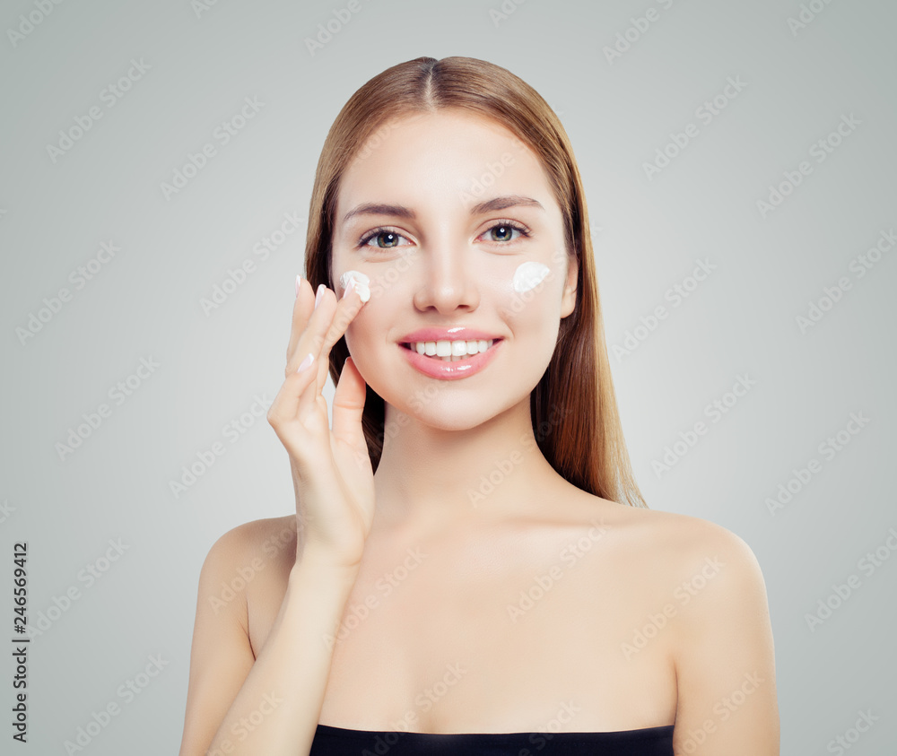 Happy beautiful woman putting cream on healthy skin. Pretty girl with natural makeup applying beauty moisture cosmetics on white background Happy beautiful woman putting cream on healthy skin. Pretty girl with natural makeup applying beauty moisture cosmetics on white background