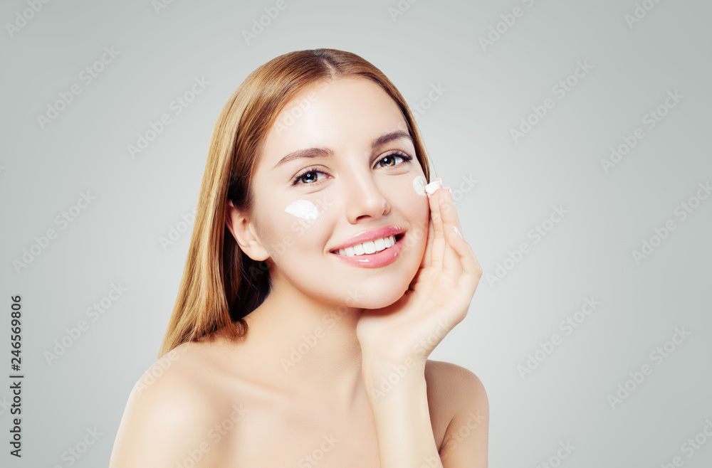 Beauty portrait of cute young woman smiling while applying some facial cream on her cheek Beauty portrait of cute young woman smiling while applying some facial cream on her cheek