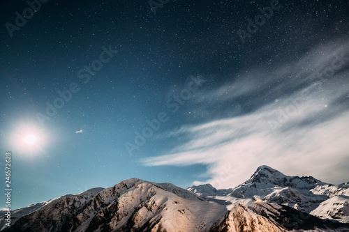 Stepantsminda, Georgia. Moonrise In Winter Night Starry Sky With Glowing Stars Over Peak Of Mount Kazbek Covered With Snow. Beautiful Night Georgian Winter Landscape