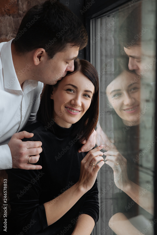 Obraz premium Happy couple of lovers sit on the windowsill. Christmas atmosphere at home. Young family together