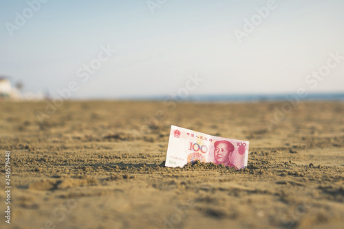 Banknote of value of of an China yuan in the the sand on the beach. Concept of cheap travel insurance