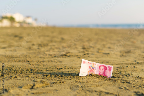 Banknote of value of of an China yuan in the the sand on the beach. Concept of cheap travel insurance