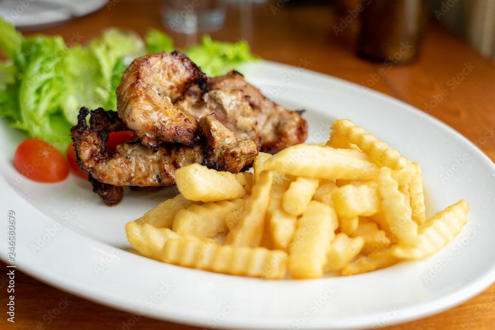 Grilled Pork and French Fries, arranged on a beautiful white food dish with salad vegetables, looking to eat Western main dishes. Popular with many