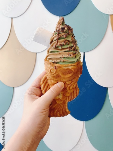 Hand with Fish shaped ice-cream with chocolate and mint creamy ice-cream on a colorful fish flakes background