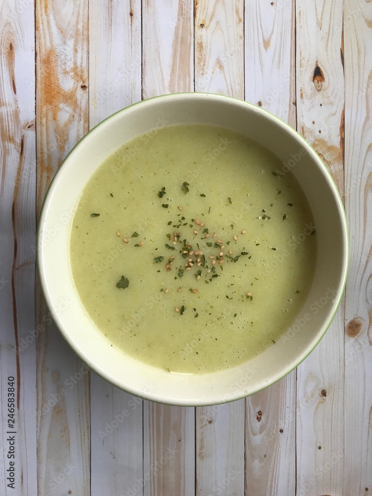 Top view of a cream soup of Zucchini and vegetables with sesame and parsley in a white bowl in a light wooden background Top view of a cream soup of Zucchini and vegetables with sesame and parsley in a white bowl in a light wooden background