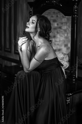 Portrait of young woman in elegant silk black dress posing in a dark interior  fashion beauty photo