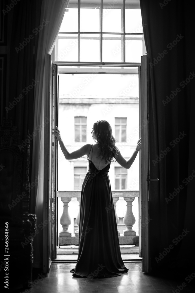 Fototapeta Czarno biały portret młodej kobiety w eleganckiej jedwabnej sukni, patrząc na miasto z balkonu