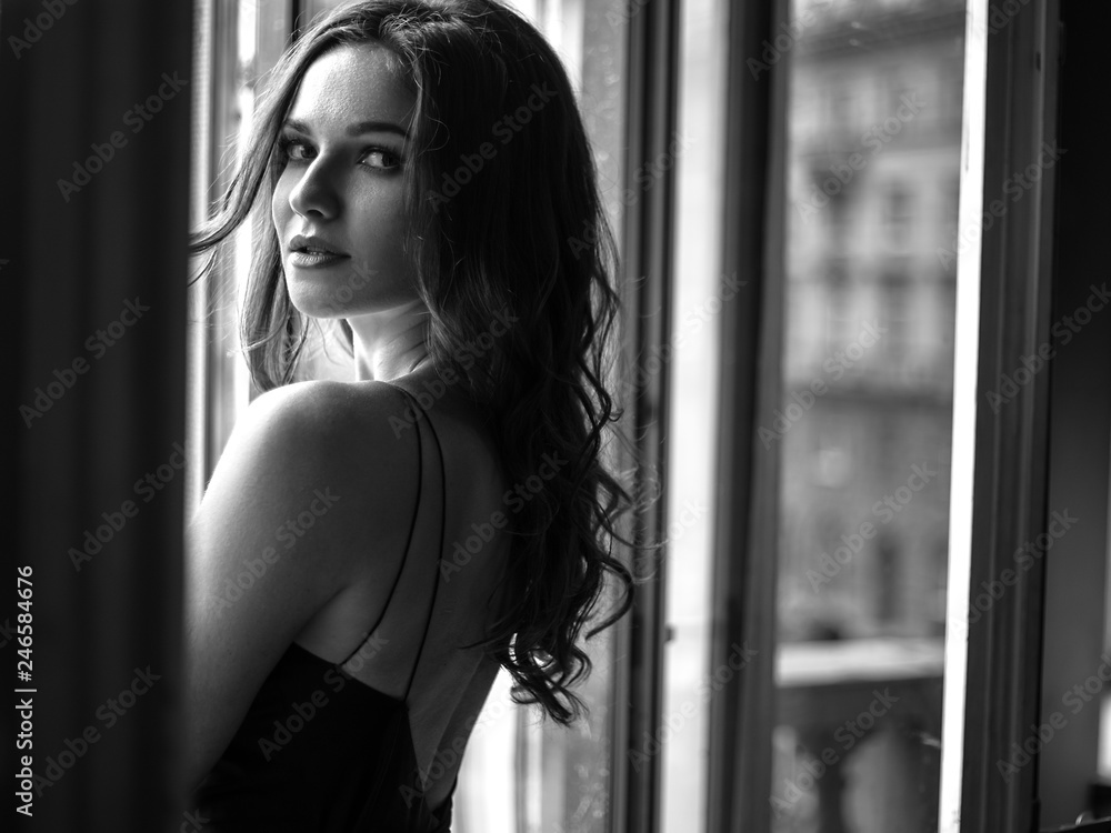Φωτογραφία Black white portrait of young woman in elegant silk black dress lookingto a city
