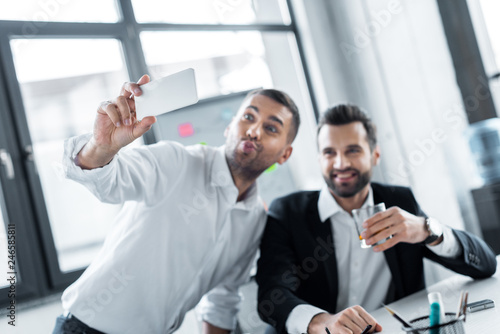 selective focus of cheerful businessmen taking selfie in modern office