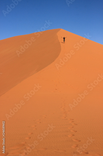 A male traveler in sportswear is standing on the orange sand of a dune in Sosusfle National Park  Namibia.