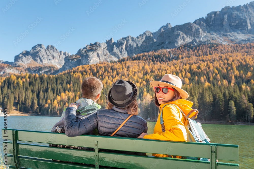 Happy three friends travel in Italian Dolomites mountains stading on the coast of a Misurina Lake
