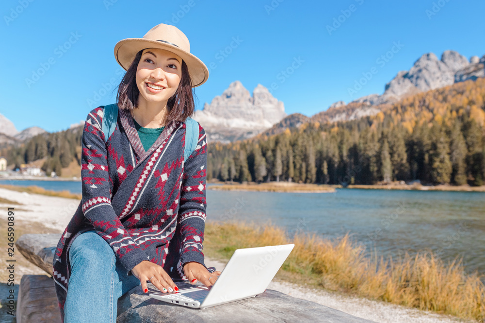 Happy Asian woman working on laptop on mountain lake background in autumn. The concept of remote work and freelancer