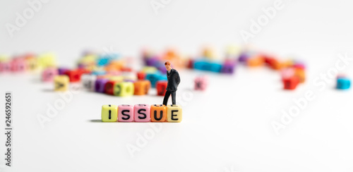 Select focus of colorful of ISSUE alphabet and looking and miniature figure businessman in dark blue suit standing behind ISSUE alphabet and thinking of ways to solve the problem.