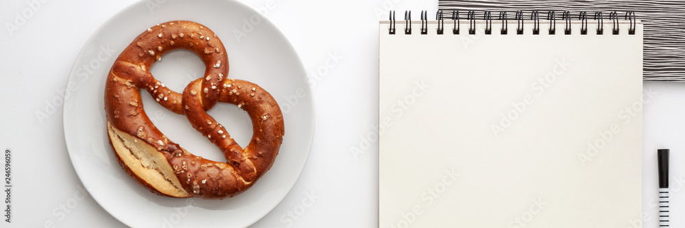 Opened empty sketchbook mockup on the desk. Top view real photo. Black-and-white concept desk with pretzel on a white plate. Panorama with place for text Opened empty sketchbook mockup on the desk. Top view real photo. Black-and-white concept desk with pretzel on a white plate. Panorama with place for text