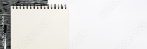 Opened empty sketchbook mockup on the desk. Top view real photo. A black and white concept desk with geometrically worn office supplies. Blank white background with space for text. Panoramic photo