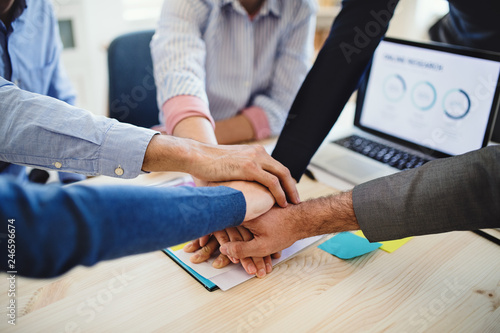 Young businesspeople sitting around table in a modern office, putting hands together.