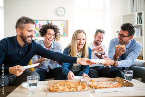 Принти на полотні Group of young businesspeople with pizza having lunch in a modern office
