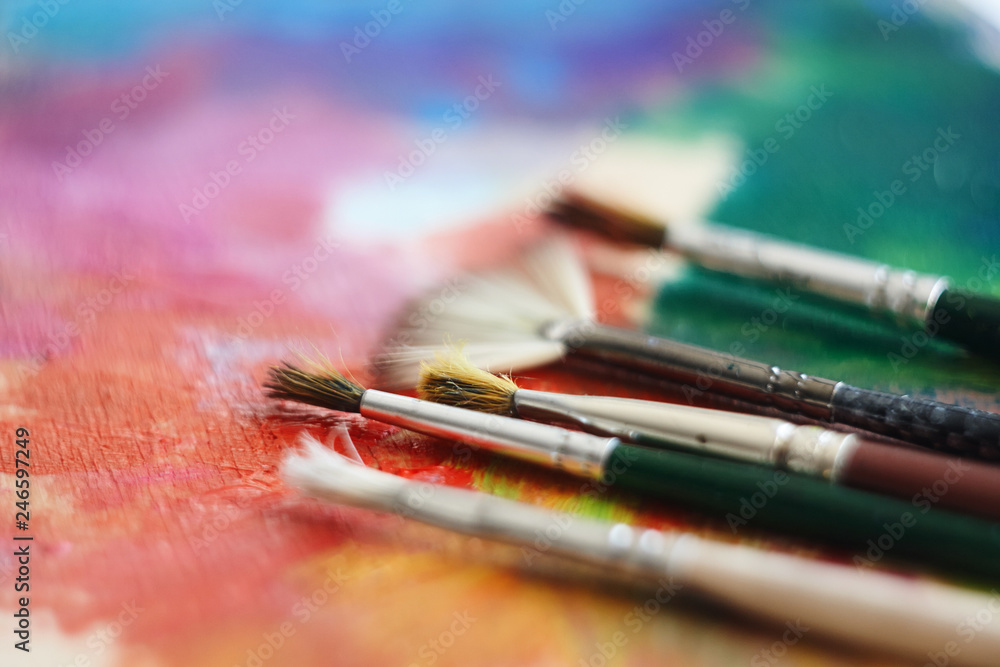 Several brushes of different shapes are on a multi-colored palette, painted with oil paints Several brushes of different shapes are on a multi-colored palette, painted with oil paints