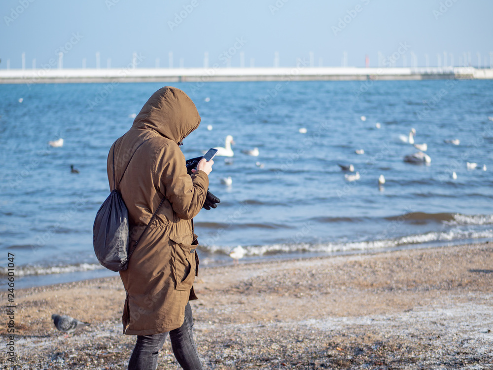 Man walking on the beach during winter season and playing with smartphone.