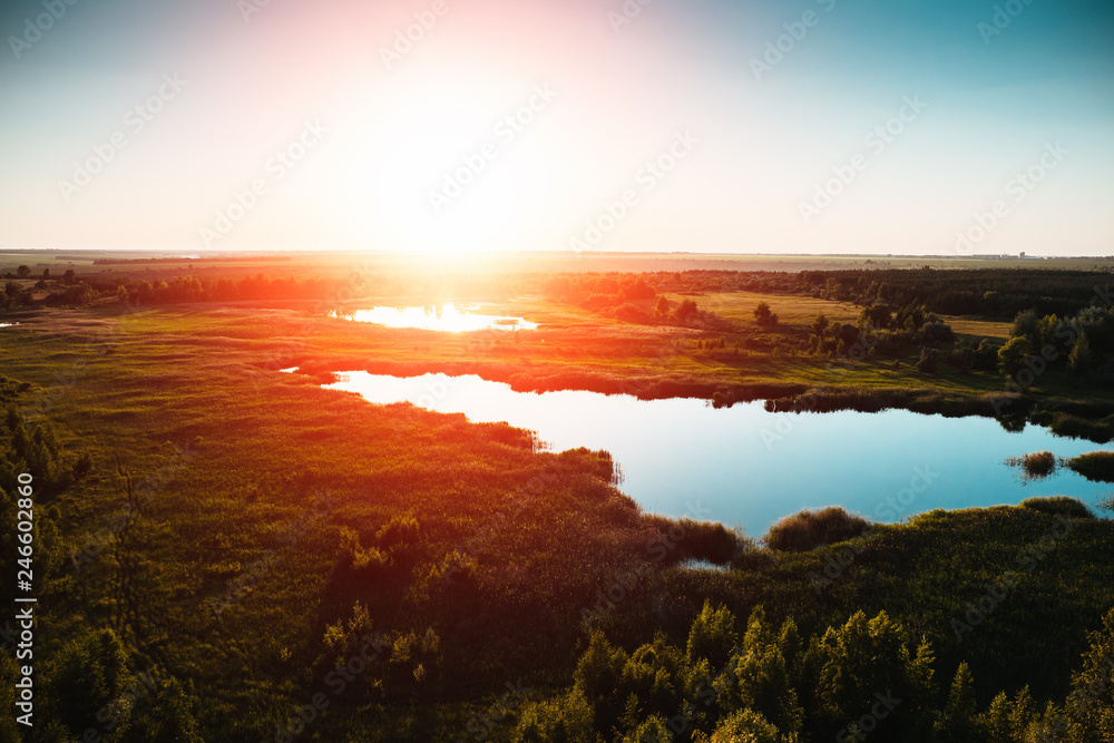 Dramatic spring nature landscape with sunset over green meadows with lake and forest