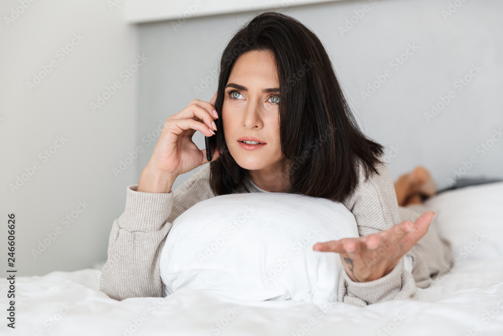 Photo of pretty woman 30s using mobile phone, while lying in bed with white linen in bright room Photo of pretty woman 30s using mobile phone, while lying in bed with white linen in bright room