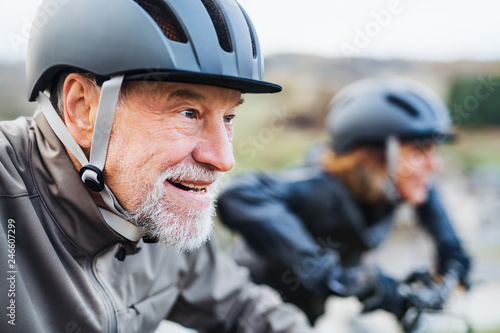 Active senior couple with electrobikes cycling outdoors on a road in nature.