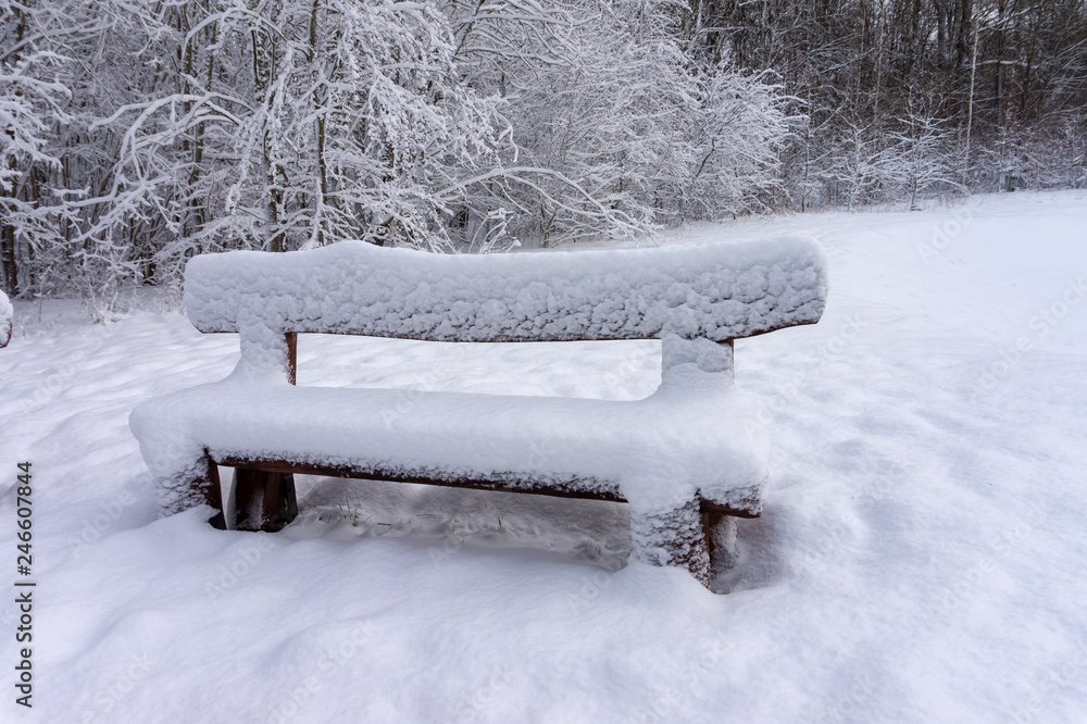 Snow-covered rustic wooden bench in a winter park