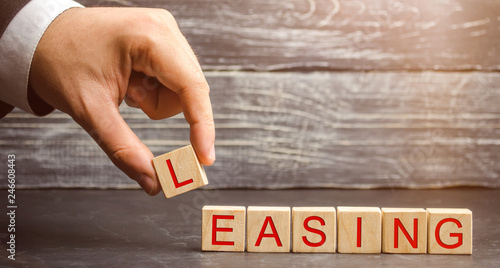 Man puts cubes with the word Leasing. A lease is a contractual arrangement calling for the lessee to pay the lessor for use of an asset. Property, buildings, vehicles are common assets that are leased photo