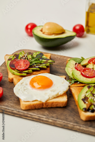 selective focus of cutting board with toasts, scrambled egg, cherry tomatoes and avocado on grey background