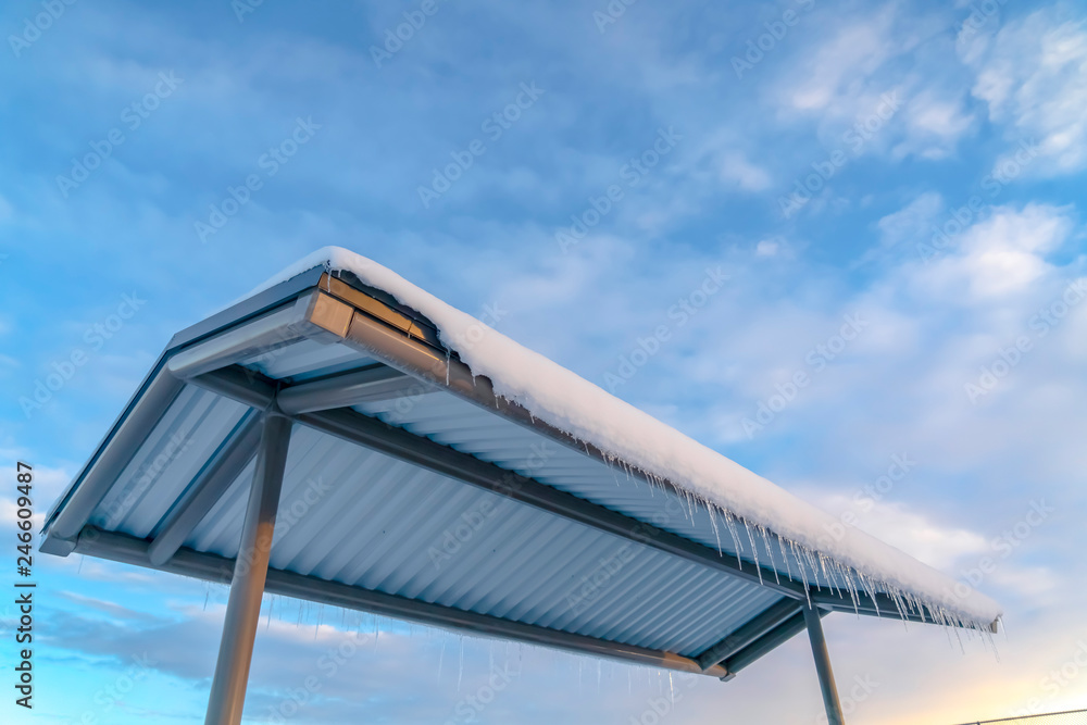 Roof with snow and icicles against cloudy blue sky Roof with snow and icicles against cloudy blue sky
