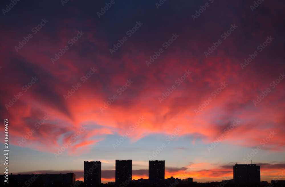 Mystical purplish red sunset over the dark silhouette of city. Incredibly beautiful cloudscape in sunset light in violet, purple, coral, blue and orange tones Mystical purplish red sunset over the dark silhouette of city. Incredibly beautiful cloudscape in sunset light in violet, purple, coral, blue and orange tones