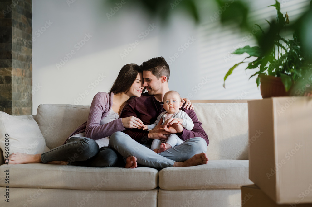 A portrait of young couple with a baby and cardboard boxes moving in a new home. A portrait of young couple with a baby and cardboard boxes moving in a new home.