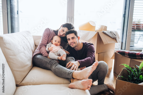 A portrait of young couple with a baby and cardboard boxes moving in a new home. photo