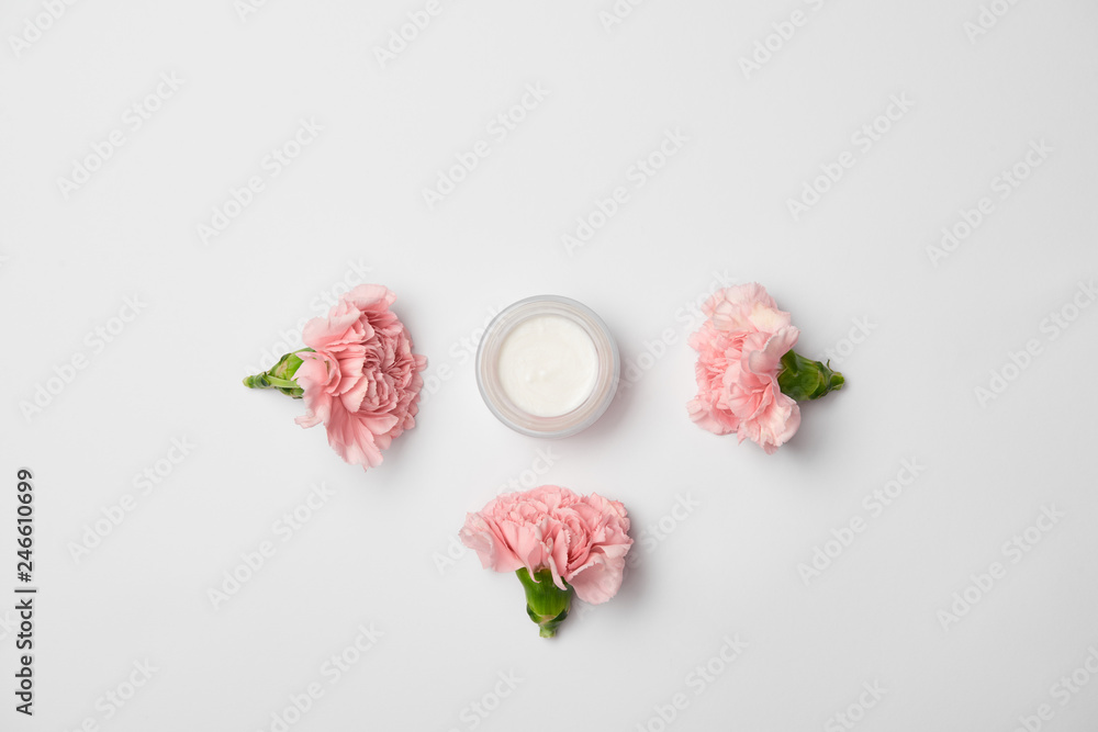 Top view of cream container and pink carnations flowers on white background Top view of cream container and pink carnations flowers on white background