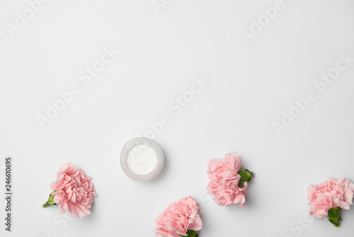 Fototapeta Naklejka Na Ścianę i Meble -  Top view of pink carnations flowers and cream container on white background