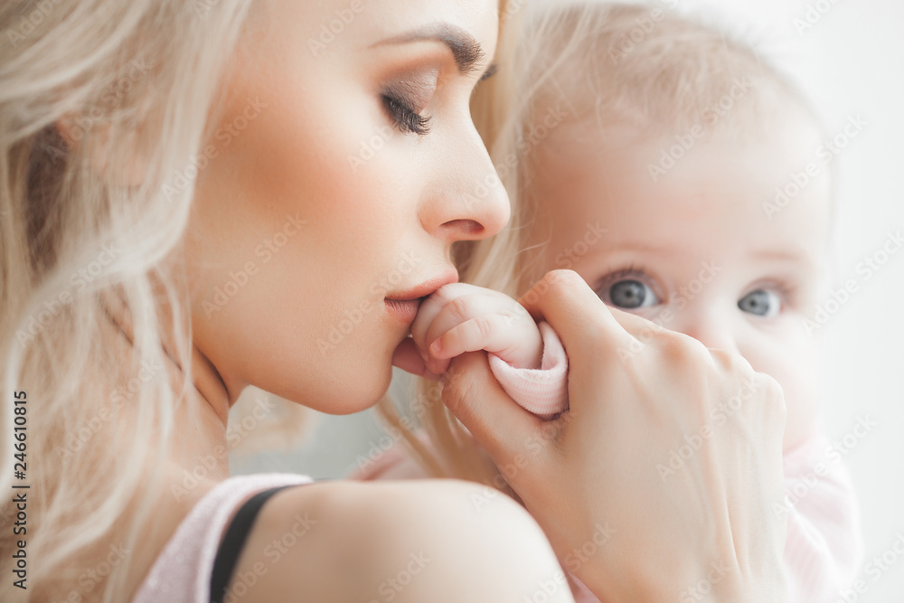 Young attractive mother kissing her baby. Mom kissing child`s little fingers. Woman care of her daughter.