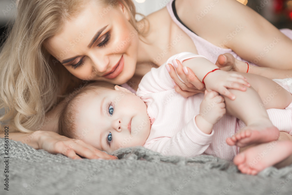 Young mother taking care of her little baby girl. Beautiful mom and her daughter indoors in the bedroom. Loving family. Attractive mum holding her child. Young mother taking care of her little baby girl. Beautiful mom and her daughter indoors in the bedroom. Loving family. Attractive mum holding her child.