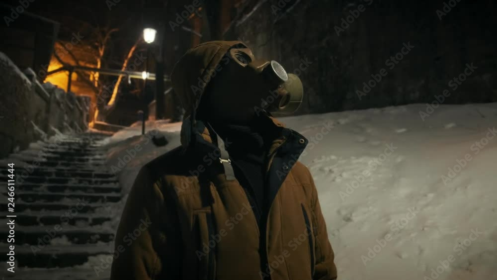 Man in gas mask standing near broken street lamp. Natural strobe light. Horror scene Man in gas mask standing near broken street lamp. Natural strobe light. Horror scene