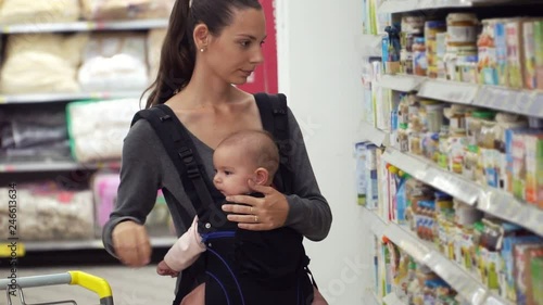 A young mother carrying her little baby in a sling carrier at a supermarket store buying baby food parenting concept