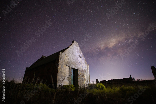 Wide angle astrophotography scene of an old abandoned building with the bright nigh sky above it.